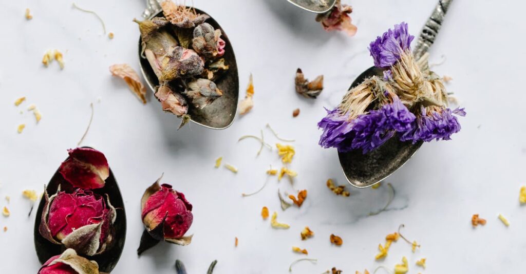 Aesthetic flat lay of vintage spoons filled with various dried herbs and flowers on a marble surface.